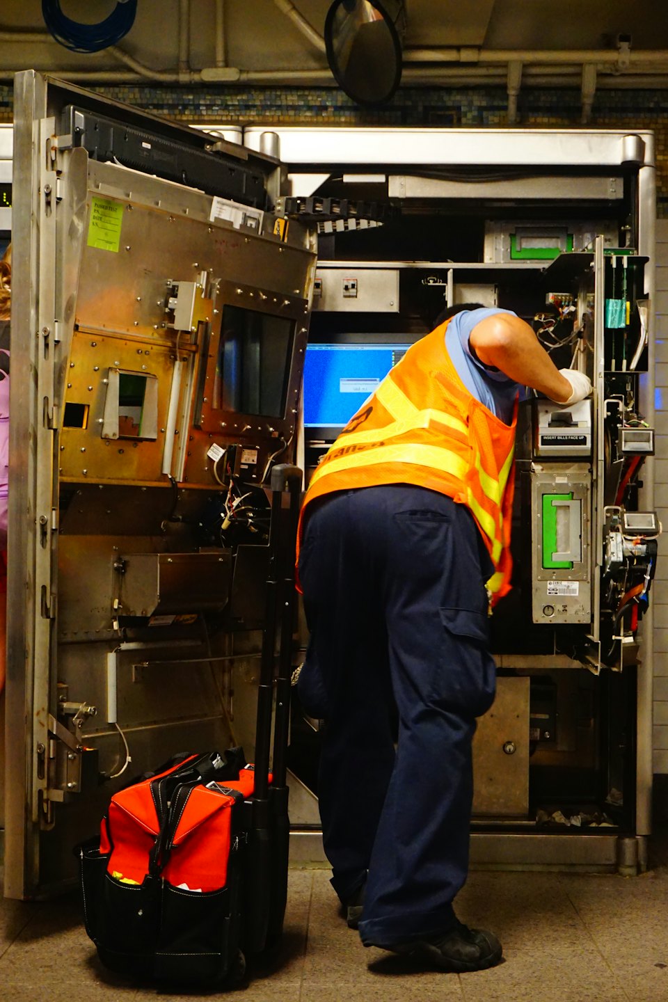 Technician in safety vest works on public service machine.
