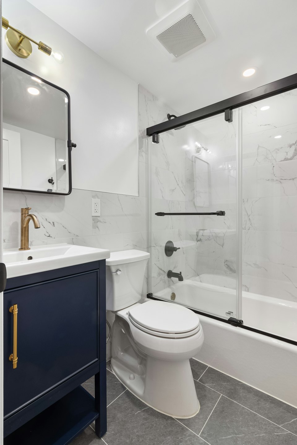 Modern bathroom with navy vanity, gold faucet, and marble tiles.