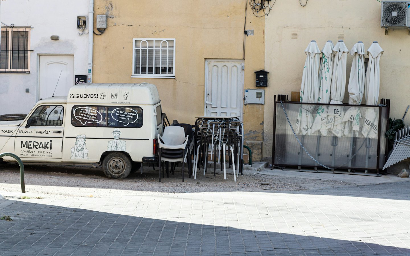 Branded delivery van parked beside stacked outdoor cafe furniture.